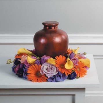 Copper urn centerpiece surrounded by orange, yellow, and purple flowers on white table at Joshua's Greenery