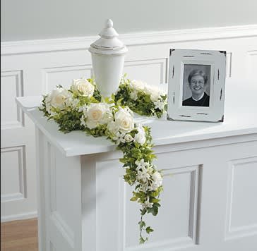 White rose funeral arrangement with greenery beside urn and framed photo on white table, Joshua's Greenery Barrie Florist