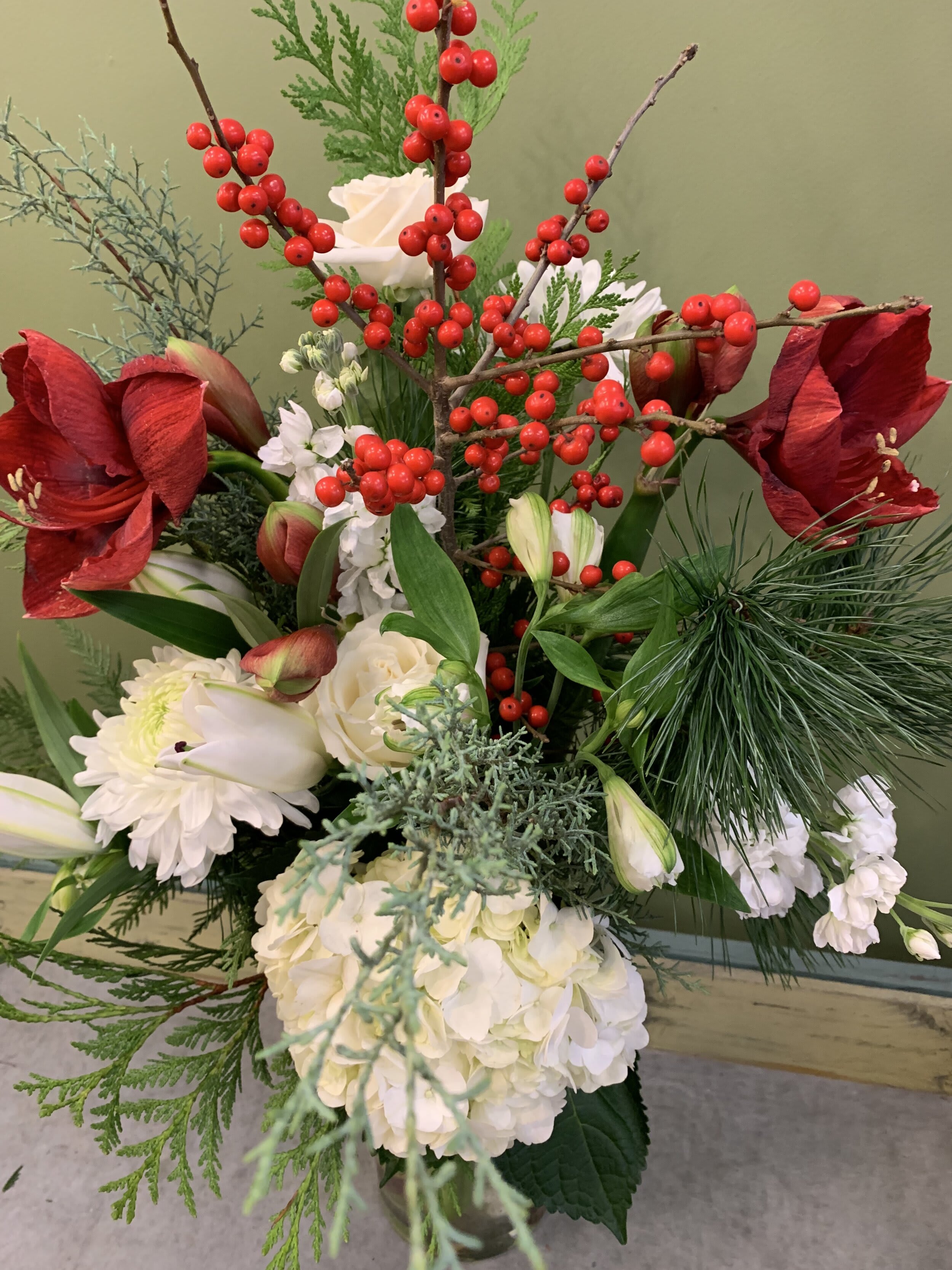 Festive flower arrangement with red amaryllis, white roses, berries and greenery by Joshua's Greenery