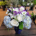 Elegant flower arrangement with white roses, blue hydrangeas, and purple blooms in a blue vase, by Joshua's Greenery Barrie Florist.