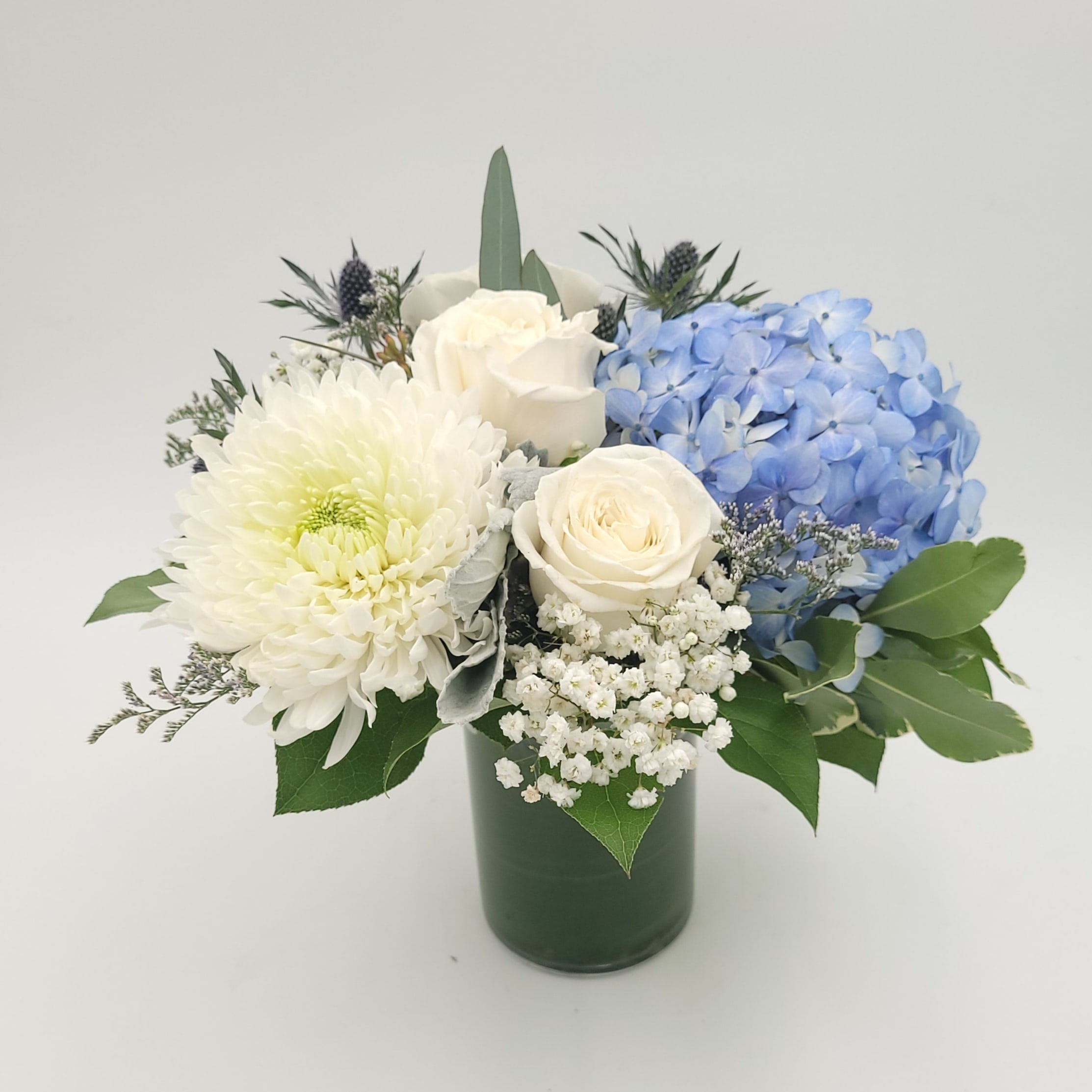 Elegant flower arrangement with white roses, blue hydrangea, and greenery in glass vase