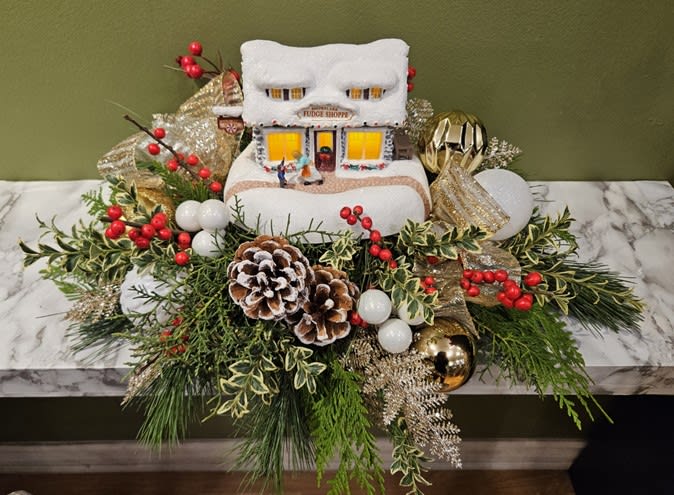 Festive holiday floral arrangement with pinecones, red berries, greenery, and a snow-covered Fudge Shoppe house decoration, designed by Joshua's Greenery Barrie Florist.