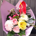 Fresh flower bouquet with pink roses, yellow peony, and red anthurium in pastel wrap