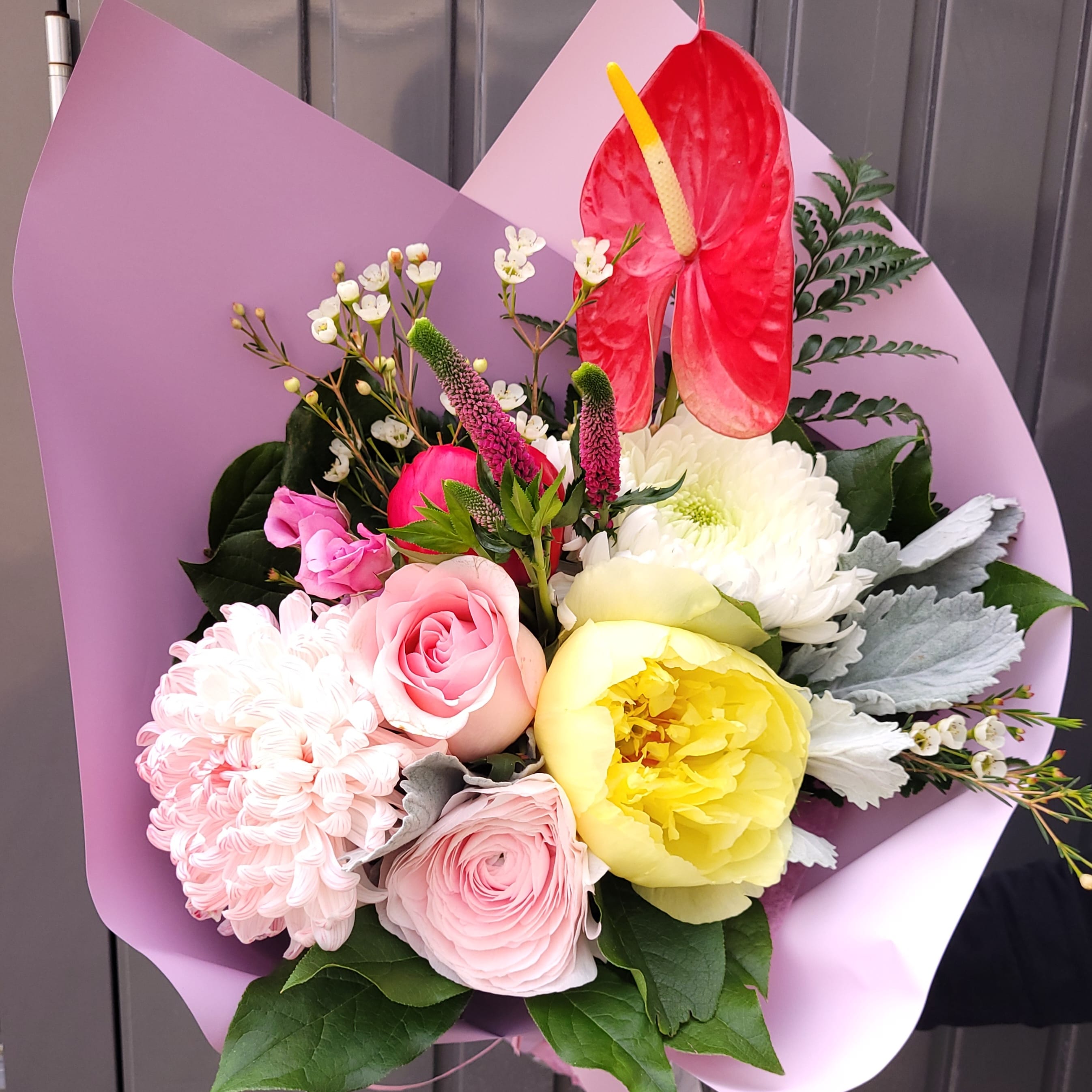 Fresh flower bouquet with pink roses, yellow peony, and red anthurium in pastel wrap