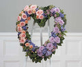 Heart-shaped floral wreath with pink roses, lavender roses, and greenery on white stand, Joshua's Greenery-Barrie Florist